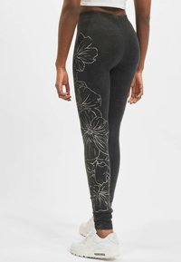 Sorte leggings med et blomster mønster i hvit linje, høy midje og elastisk stoff, kombinert med hvite treningssko.
