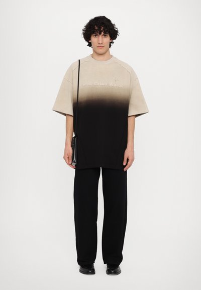Tricou supradimensionat cu gradient, de la bej la negru, având un logo brodat. Asortat cu pantaloni largi negri și o geantă micuță de umăr neagră.