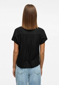 Blusa nera a maniche corte con dettaglio arricciato sul retro, abbinata a jeans chiari a vita alta. Tessuto morbido e leggero.