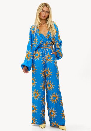 Conjunto de dos piezas azul con un patrón de sol. La parte superior tiene un escote en V profundo y un diseño fruncido. Los pantalones de pierna ancha tienen una cintura elástica.