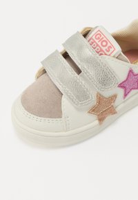 Hvit sneakers med metallisk sølv og beige detaljer, med borrelåsremmer og tre glitrende stjerneapplikasjoner i rosa og gull.