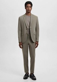 Licht olijfgroen pak met een getailleerde blazer en taps toelopende broek. Draag het over een lichtgrijs overhemd en in combinatie met zwarte leren schoenen. Soepele textuur.