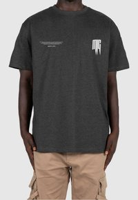 Camiseta de algodón gris oscuro con mangas cortas, que presenta texto blanco en la parte posterior y un pequeño gráfico blanco en el pecho. Diseño limpio y casual.