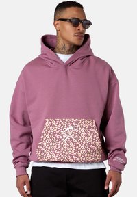 Pink hoodie with a large leopard print pocket, featuring white accents. The fabric appears soft with a relaxed, oversized fit.
