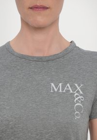 Camisa gris de manga corta hecha de tela suave, con un pequeño logo blanco en el lado izquierdo. Cuello clásico de estilo crew y textura lisa.