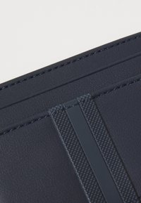 Navy blue leather piece with textured accents, two horizontal stripes, and evident stitching detail. Smooth finish with a subtle sheen.