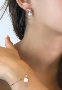 Orecchini in oro rosa con goccia di perla e accenti di cristallo; bracciale con una singola perla su una delicata catena.