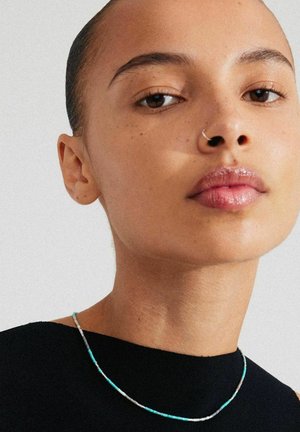 Fine beaded necklace featuring turquoise and silver accents, worn over a black top. Smooth texture, minimalistic design with a delicate look.