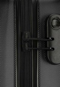 Valigia nera con texture in primo piano, dotata di una zip liscia, hardware in plastica e cuciture rinforzate per una maggiore durata. Due tiri della zip sicuri sono visibili.