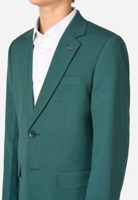 Blazer teal con chiusura a un solo bottone, con lapels a punta e taschino sul petto. Presenta un piccolo accento ricamato sul colletto.