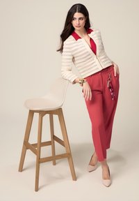 Completo femminile composto da una giacca a righe crema con colletto rosso, abbinata a pantaloni a vita alta rossi. Un paio di semplici décolleté beige completano il look.