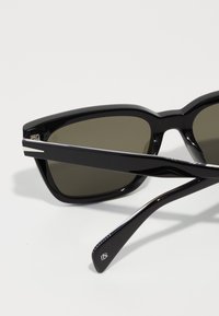 Ochelari de soare negri cu rame unghiulare, lentile verde închis și accent argintiu pe tâmple. Finisaj lucios și brațe conice pentru un design elegant.
