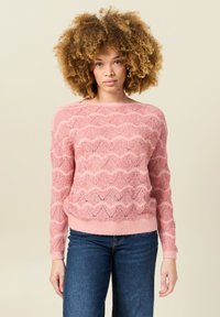 Rosa Strickpullover mit gewelltem Muster, gerippten Bündchen und Saum sowie lockerer Passform. In Kombination mit blauen Jeans wirkt die Textur weich und leicht.