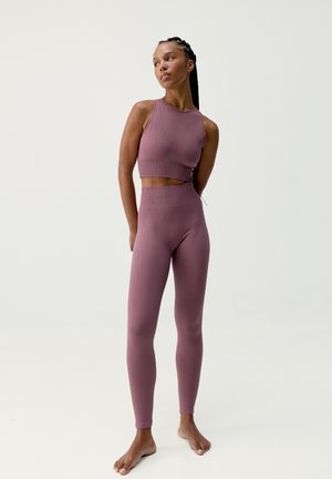 Conjunto de sujetador deportivo y mallas en color malva, de tela acanalada. El sujetador presenta un cuello alto; las mallas tienen una cintura alta y un diseño ajustado.