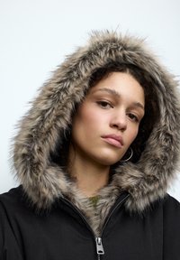 Czarna kurtka z kapturem wykończonym sztucznym futerkiem w odcieniach beżu i brązu. Posiada srebrny zamek błyskawiczny oraz prążkowany, dziany kołnierz. Gładka tekstura.