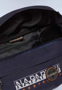 Borsa in tessuto blu navy con chiusura a zip, caratterizzata da un interno nero, un'etichetta con logo arancione e bianco, e dettagli di cucitura a contrasto.