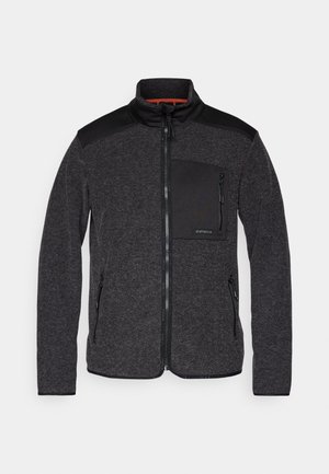 Musta fliisjakker kõrge kaelusega, lõppenud lukuga ja lukuga rinnataskuga; omaduseks on kontrastne mustad õlapaneelid. Pehme tekstuur.