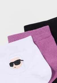 Tre paia di calzini: bianchi con un volto ricamato, rosa e neri. I calzini rosa e neri hanno una finitura a maglia testurizzata.