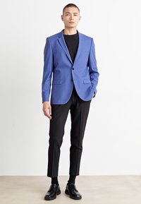 Sacou bleumarin, ajustat, cu un singur nasture, rever în formă de vârf și două buzunare frontale, asortat cu pantaloni negri, ajustați și pantofi de birou negri.
