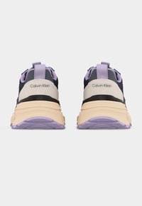 Ζευγάρι αθλητικά παπούτσια Calvin Klein, ορατά από πίσω, με μαύρες, μπεζ και μοβ λεπτομέρειες, και χοντρές μπεζ σόλες με μοβ πέλμα.