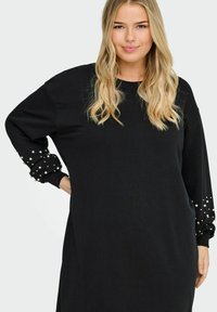 Robe-sweat noire à manches longues avec des poignets texturés ornés de perles. Tissu doux et coupe décontractée.