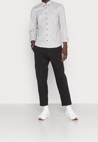 Camicia a quadri grigia con bottoni neri, abbinata a pantaloni neri tapered e sneakers bianche con dettagli arancioni.
