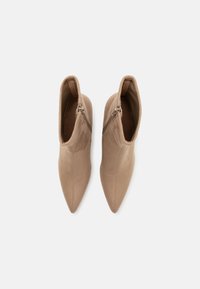 Bottines à bout pointu en tissu beige lisse, avec une fermeture éclair latérale visible et un design ajusté qui épouse la cheville.