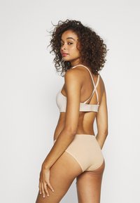 Beige beha en hoge taille ondergoedset in geribbelde textuur, met verstelbare banden en een haak-en-oogsluiting aan de achterkant.
