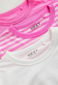 Tri presavijene majice NEXT marke s okruglim izrezom: jednobojna ružičasta, ružičasto-bijele pruge i jednobojna bijela.
