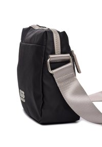 Bolso negro de nailon tipo bandolera con forma rectangular, detalles en plata y una correa texturizada. Presenta un cierre superior con cremallera y un detalle del logo.