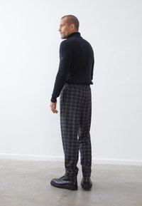 Pull à col roulé côtelé marine, pantalons à motif gris à carreaux et chaussures à lacets noires. Textures lisses avec des silhouettes ajustées.