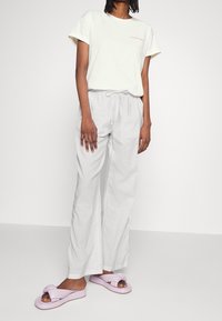 T-shirt crème à manches courtes avec du texte violet, assortie à un pantalon ample gris clair à cordon de serrage et des sandales lilas avec un nœud.