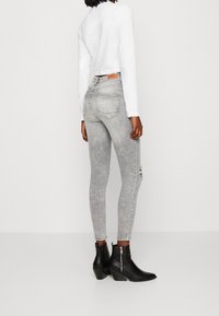 Šedé úzké džíny s vybledlým efektem a mírným opotřebením, doplněné o černé kotníkové boty se zipem.