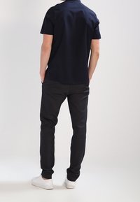 Chemise courte à manches en marine avec un col, associée à un pantalon noir ajusté et des baskets blanches. Le tissu semble lisse et décontracté.