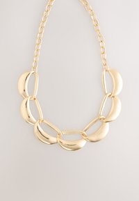 Goudkleurige ketting met gebogen halvemaanvormige schakels en langwerpige verbindingschakels, afgewerkt met een gladde, reflecterende textuur.