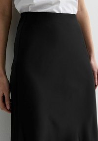 Jupe crayon noire en tissu lisse. Présente une taille haute et une coupe droite, mettant en avant un design épuré et minimaliste.