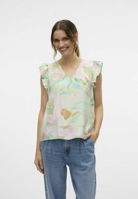 Gaismas, piparmētru zaļš blūze ar V-veida kakla izgriezumu, viļņotām piedurknēm un pasteļozāku ziedu rakstiem. Kombinēta ar brīviem, ziliem džinsiem.