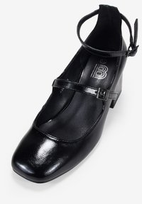 Scarpa Mary Jane in finta pelle nera con punta arrotondata, cinturino alla caviglia e tacco basso. L'interno presenta una superficie liscia con branding.