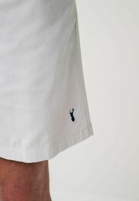 Hvide bomuldsshorts med en subtil tekstur, der har et marineblåt hummerlogo ved kanten og en ren, lige skæring langs bunden.