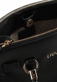 Zwarte leren handtas met gouden ritsen en hardware. De binnenzijde heeft een patroonvoering. Opvallend ringaccent aan de buitenkant.