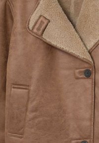 Chaqueta de gamuza marrón con forro de felpa beige claro, cuello ancho, cierre de botón y detalle de bolsillo frontal rectangular.