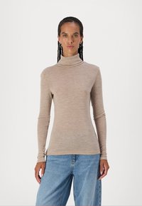 Lys beige turtleneck topp laget av myk stoff, med lange ermer og en tettsittende design, kombinert med vide blå jeans.