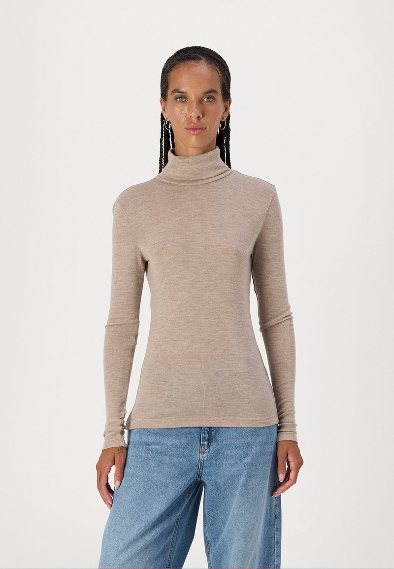 Lys beige turtleneck topp laget av myk stoff, med lange ermer og en tettsittende design, kombinert med vide blå jeans.