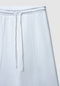 Pantalon de survêtement blanc avec une taille élastique et un cordon de serrage. Fabriqué en tissu doux, il présente deux coutures verticales sur chaque jambe.