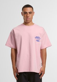 Pink cotton t-shirt with a relaxed fit, featuring blue text on the chest and short sleeves. Simple, crew neck design.