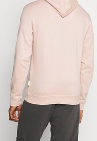 Sudadera rosa clara confeccionada en un tejido texturizado, con capucha ajustable y puños acanalados. Decorada con una pequeña etiqueta en el costado.