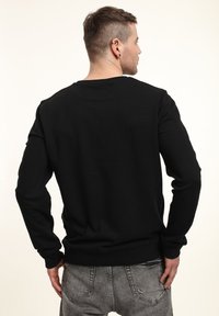 Černá mikina s dlouhými rukávy, žebrovanými manžetami a lemem. Měkká textura, standardní střih a minimalistický design bez log a ozdob.