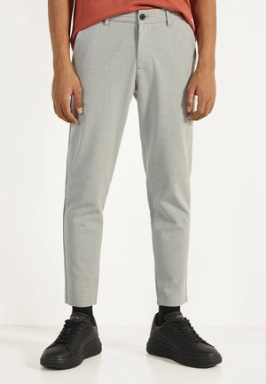 Lichtgrijze taps toelopende broek van een geweven stof. Slank fit ontwerp, met een knoopsluiting en zijzakken. Gepaard met zwarte sneakers.