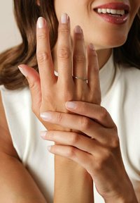 Silver ring med gröna stenar bärs på en hand med välvårdade, ljusa naglar. Fingrarna är försiktigt sammanslutna mot en ljus bakgrund.