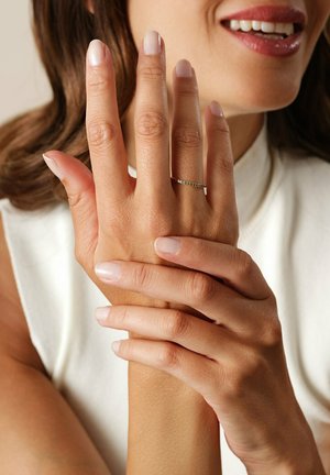 Sølvring med grønne sten båret på en hånd med pænt manicurede, lyse negle. Fingrene er blidt samlet mod en lys baggrund.